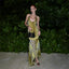 Woman in a yellow and black patterned dress standing against a green leafy background