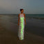 Woman in a glowing dress standing on a beach at dusk