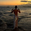Woman in a white dress standing in the water at sunset