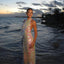 Woman in a sparkling dress standing by the water at sunset