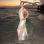 Woman in a floral dress standing in shallow water at sunset on a beach.