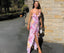 Woman in a floral dress standing against a brick wall.