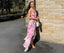 Woman in a floral dress standing against a brick wall.