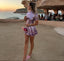 Woman in a sequin dress standing on a sandy beach with ocean and cliffs in the background.