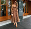 Woman in a leopard print dress standing outside a building with wooden doors.